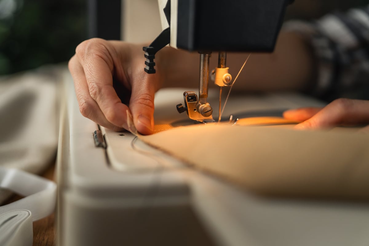 Hands guiding fabric under an electric sewing machine needle, home tailoring and craftsmanship