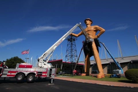 Giant inflatable firefighter statue with fire truck parked nearby under clear blue sky