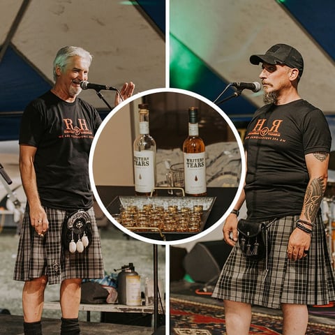 Two men in kilts at a whiskey tasting event, with bottles and glasses displayed in the center circle