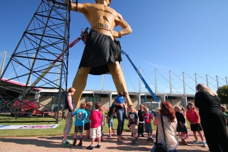 Giant muscle man statue with visitors viewing below at a sports stadium or public venue