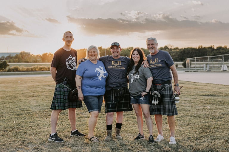 Five people wearing tartan kilts and t-shirts standing together on a soccer field at sunset