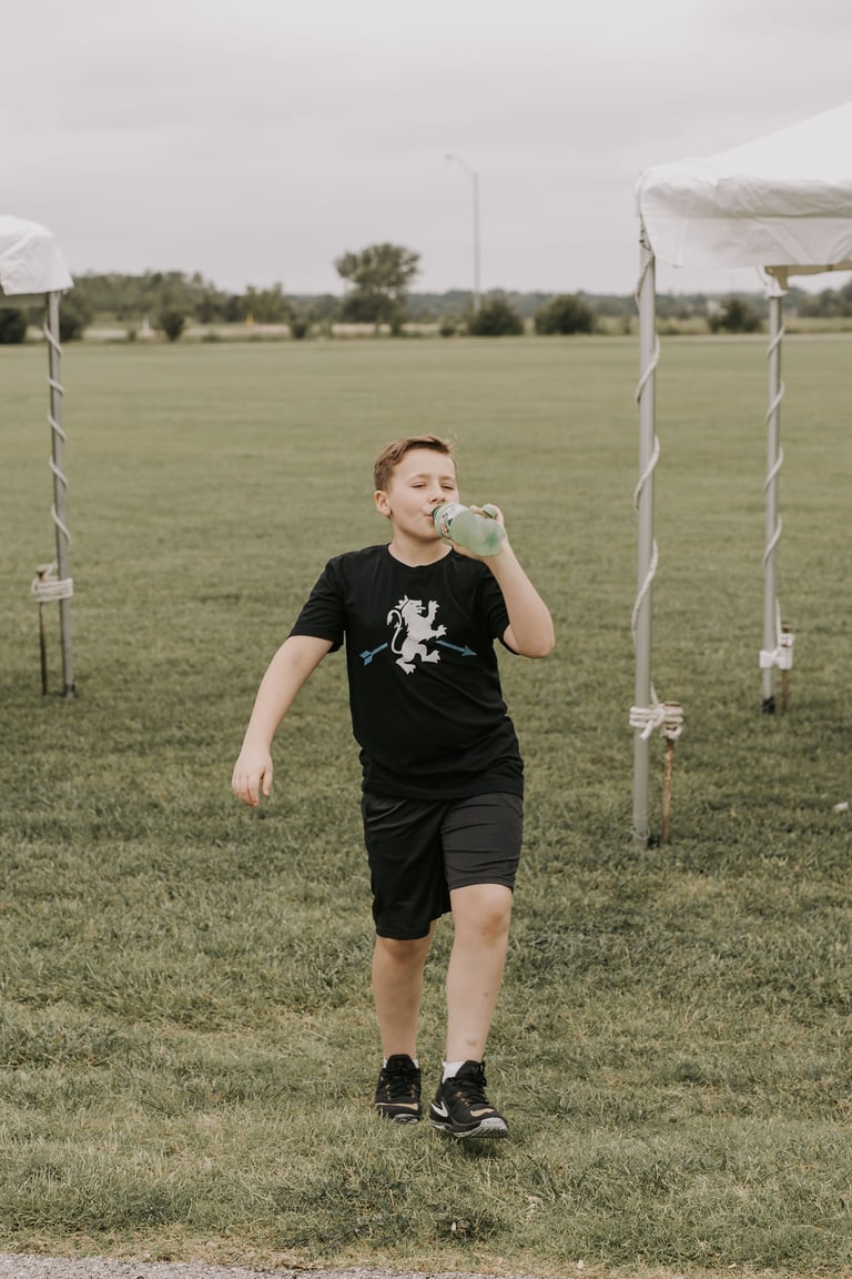 Young boy running through a sports field while drinking from a water bottle, with goal posts visible in the background